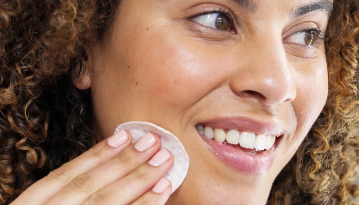 Image of woman smiling and using Neora’s Complexion Treatment Pads on her face